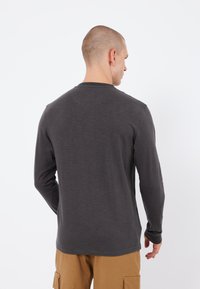 Long-sleeve shirt in dark gray fabric with a round neckline and soft texture. Features a simple design with no visible patterns or accents.