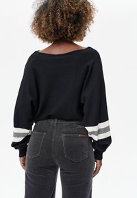 Zwarte gebreide trui met off-shoulder ontwerp en witte gestreepte accenten. Gecombineerd met donkergrijze corduroy broek met achterzakken.