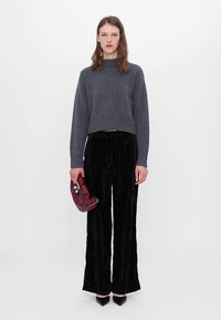 Pull gris court avec ourlet côtelé, associé à un pantalon large en velours noir. Le mannequin tient un sac bordeaux et porte des chaussures noires à bouts pointus.