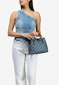 Sac en denim avec un motif géométrique bleu, des accents beige, et une forme structurée. Le sac possède des poignées courtes de style bambou.