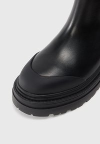 Stivale alla caviglia in pelle nera con punta arrotondata, gambale texturizzato e suola spessa in gomma con un motivo testurizzato per la presa.