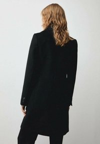 Palton lung, negru, fabricat dintr-un material moale, având o siluetă dreaptă, guler tip notch și manșete cu nasturi, văzut din spate.