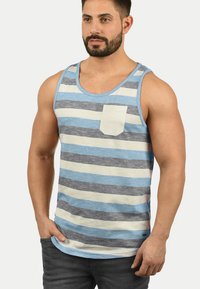 Gestreepte tanktop in blauw, grijs en crèmekleur, met een zak op de linkerborst. Gemaakt van lichtgewicht stof, met een ronde hals en mouwloos ontwerp.