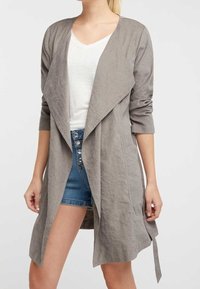 Chaqueta gris, ligera, de frente abierto con mangas largas y un cuello drapeado. Presenta un detalle de lazo en la cintura y una tela texturizada.