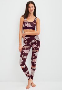 Floral sportbeha en legging set in donker bordeauxrood met lichtroze en crème bloemenpatronen; rekbare stof en strakke pasvorm.