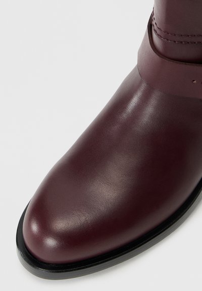 Maroon leather ankle boot with a smooth texture, rounded toe, and black sole. Features a narrow strap around the ankle.