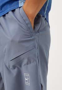 Pantalons de sport bleu clair avec une texture lisse, dotés d'une poche latérale et d'un logo Nike blanc sur la jambe inférieure.