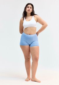 Un reggiseno sportivo bianco a coste e pantaloncini aderenti azzurri su un modello in piedi. Tessuto morbido con una texture liscia, senza motivi o design visibili.