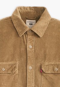 Lichtbruine corduroy overhemd met een puntige kraag, twee voorkwabben en een klein rood label aan de zijkant. Voorzien van een knoopsluiting en ribbelstructuur.