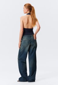 Jeans in denim blu con una vestibilità ampia, caratterizzati da un alto vita, tasche posteriori e una leggera scoloritura. La parte superiore è un modello a halter neck blu navy.