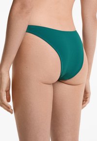 Chilot de bikini verde cu design high-cut și acoperire minimă. Prezintă cusături netede și o textură moale a materialului.