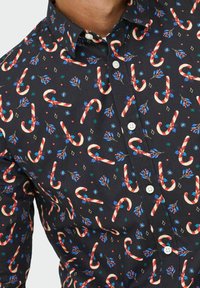 Must mustroheline särk musta taustaga, millel on punased ja valged kommipulgad, sinised friiksid ja väikesed rohelised tähed ning teemandi mustrid.