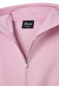 Felpa zip con cappuccio rosa con zip in metallo, morbido al tatto, e un'etichetta nera che mostra "Utopia" e la taglia "Small" all'interno del colletto.
