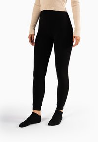 Zwarte leggings van een rekbare stof met een hoge tailleband, met een gladde textuur en een ontwerp tot aan de enkels. Draagt zwarte sokken.