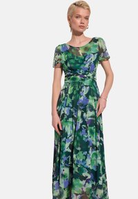 Maxi sukienka z przezroczystej zielonej tkaniny z kwiatowym wzorem w niebieskie i purpurowe akcenty, krótkie rękawy i plisowany dół.