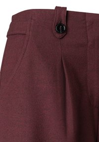 Burgunderfarbene maßgeschneiderte Hose aus glattem, strukturiertem Stoff, mit schrägen Taschen und einem schwarzen Knopfverschluss am Bund.