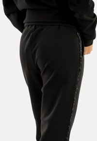 Pantalones deportivos negros con cintura elástica, textura suave y detalles laterales con un sutil estampado de leopardo.