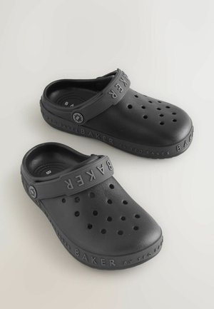 Sorte gummitræsko med en perforeret design, der har en bred rem præget med "BAKER" og et rundt logo. Tekstureret overflade.