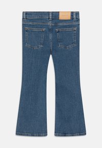 Jean flare en denim bleu avec taille haute, cinq poches et une étiquette en cuir à l'arrière. Coupe droite de genoux en bas.