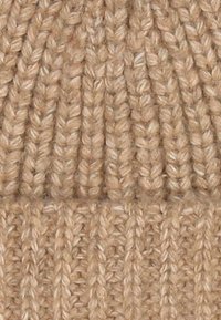 Knit beanie made of tan yarn, featuring ribbed texture with vertical lines and a folded cuff. Soft, warm appearance.