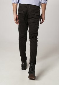 Schwarze Baumwollhosen im Slim Fit, mit zwei Gesäßtaschen und flachem Vorderdesign. Kombiniert mit schwarzen Schuhen und einem hellblauen Hemd.