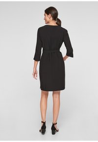 Robe noire à manches trois-quarts et taille ceinturée. Présente une texture lisse et une coupe mi-genoux, se terminant par des fentes sur les côtés.