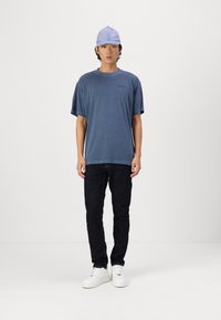 Blå bomull t-skjorte med korte ermer, avslappet passform. Kombinert med svarte jeans og hvite sneakers; toppet med en lys lilla caps.