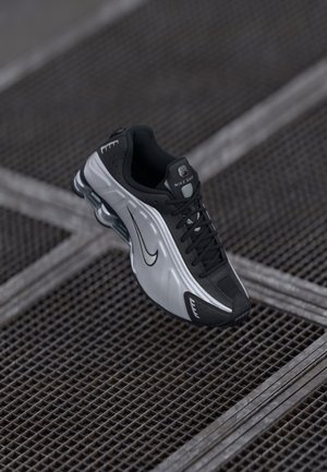 Sportowe buty Nike o czarnym i srebrnym wzorze. Wykonane z materiałów syntetycznych z siateczkowymi akcentami oraz wspierającą podeszwą z widoczną poduszką powietrzną.