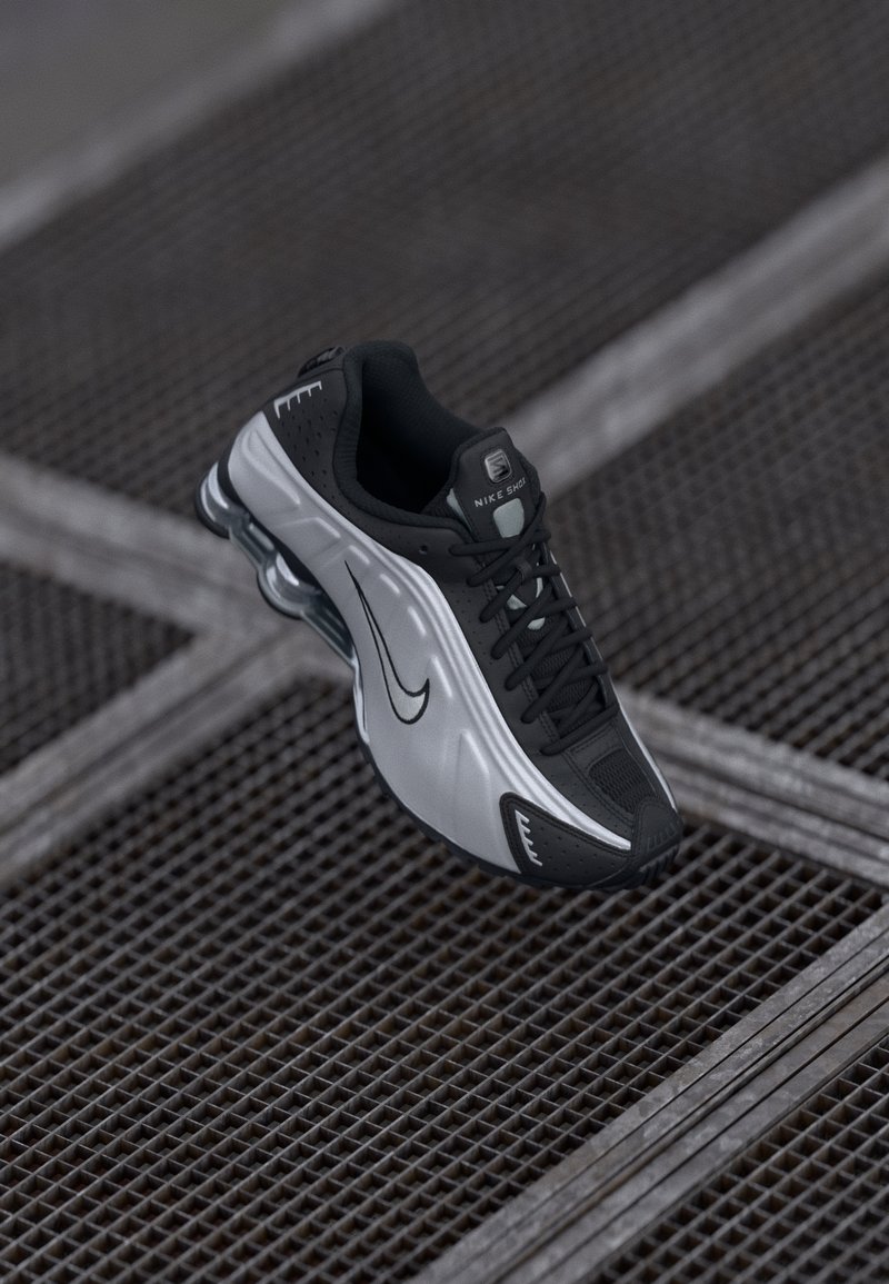 Nike atletska cipela s crno-srebrnim dizajnom. Izrađena je od sintetičkog materijala s mrežastim naglascima i potporom kroz soles s vidljivim zračnim jastučićima.
