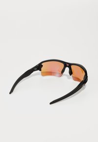 Óculos de sol desportivos com um aro preto brilhante, lentes com tonalidade laranja e design curvado. Apresenta almofadas de nariz em borracha e hastes finas e curvadas.