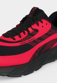 Μαύρο και κόκκινο παπούτσι για τρέξιμο Under Armour με επάνω μέρος από δίχτυ, μαύρα κορδόνια και χοντρή μαύρη σόλα, με σήμανση στο πλάι και στη γλώσσα.