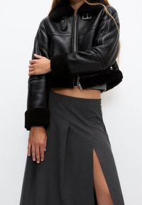 Giubbotto in pelle nera corto con collo e polsini in shearling. Gonna grigia con alta spaccatura e design strutturato.