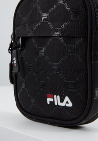 Czarna torba nylonowa z wypukłym sześciokątnym wzorem. Posiada logo Fila w kolorze białym i czerwonym. Zapięcie na suwak i teksturowana powierzchnia.