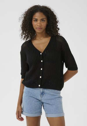Black knitted cardigan with short sleeves, V-neck, and white buttons. Features an open, breathable texture with a slightly oversized fit.