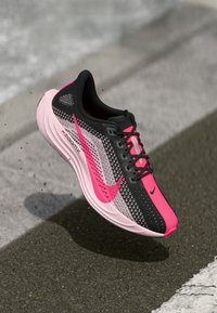 Chaussure de course Nike avec un design noir, rose et gris, dotée d'un dessus texturé et d'accents de logo distinctifs. Semelle légère pour l'agilité.