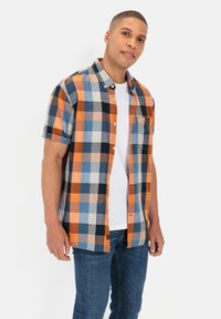 Korte mouwen, geruite overhemd in oranje, blauw en zwart. Heeft knoopsluiting, een kraag en een borstzak. Draag het over een wit T-shirt.