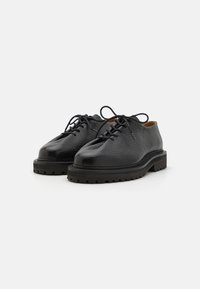 Chaussures noires en cuir à lacets avec un dessus texturé, un bout arrondi et une semelle en caoutchouc épaisse présentent un motif de traction pour une meilleure adhérence.