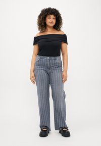 Top preto sem alças, calças de cintura alta cinza riscada com listras azuis e brancas, e sapatos plataforma pretos grossos.