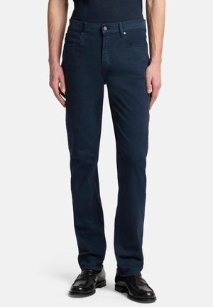 Dark blue denim jeans with a slim fit, five-pocket design, front button closure, and subtle stitching detail. Worn with black dress shoes.