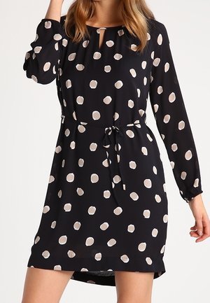 Robe noire à manches longues, encolure ronde et détail en forme de trou de serrure. Présente une taille à cordon et un motif circulaire blanc sur toute la surface.