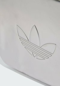 White bag with an embossed logo featuring three leaf shapes and three horizontal stripes, creating a textured and clean design.