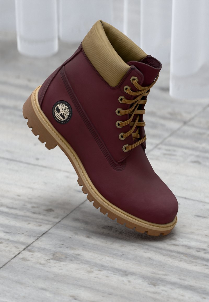 Bota de cuero marrón con cuello de tela beige, ojales metálicos y suela de goma beige. Presenta un parche de marca en el lado exterior.