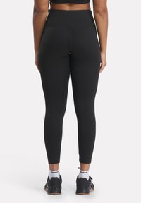 Leggings neri a vita alta caratterizzati da un tessuto elastico, una texture liscia e un design aderente, che si stringe alla caviglia. Adatti per l'abbigliamento sportivo.