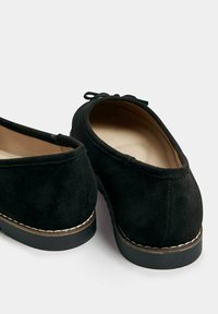 Svarta mockaskor med rund tå, platt gummisula och sömdetalj längs kanten. Slips detaljer baktill som dekoration.