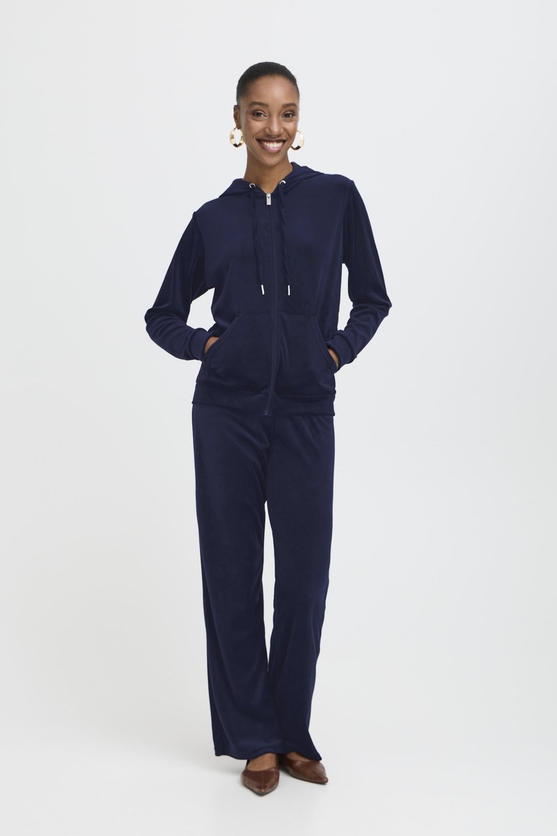 Marineblå velour-träningsdräkt som har en zip-up hoodie med framfickor och matchande vida byxor. Utformad för komfort och rörelsefrihet.