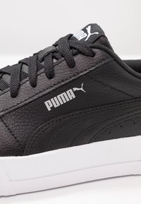 Black sneaker made of textured leather, featuring a white rubber sole, black laces, and a prominent white Puma logo on the side.