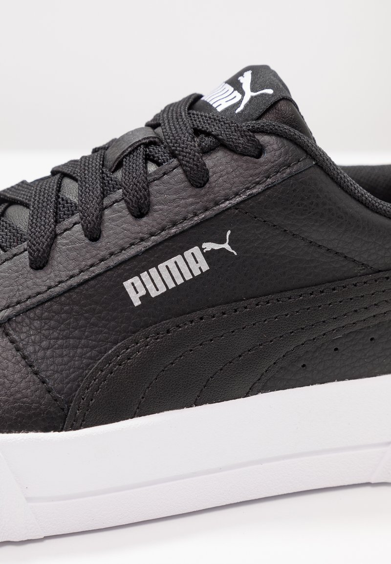 Bottines noires en cuir texturé, avec une semelle en caoutchouc blanche, des lacets noirs et un logo Puma blanc bien en vue sur le côté.