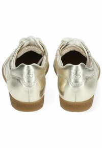 Zlaté metalické tenisky s texturovaným povrchem, mají zaoblenou zadní část, světle krémové tkaničky a gumové podrážky s ražením "paul green."