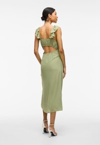 Rochie midi de nuanț�ă verde măslinie cu bretele volanate, design cu spate deschis și talie elastică. Textură fină și material fluid. Sandale cu toc înalt.
