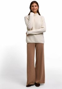 Maglione a collo alto a coste crema con maniche lunghe, abbinato a pantaloni larghi marroni a gamba larga. Il maglione ha una vestibilità comoda e una texture morbida.
